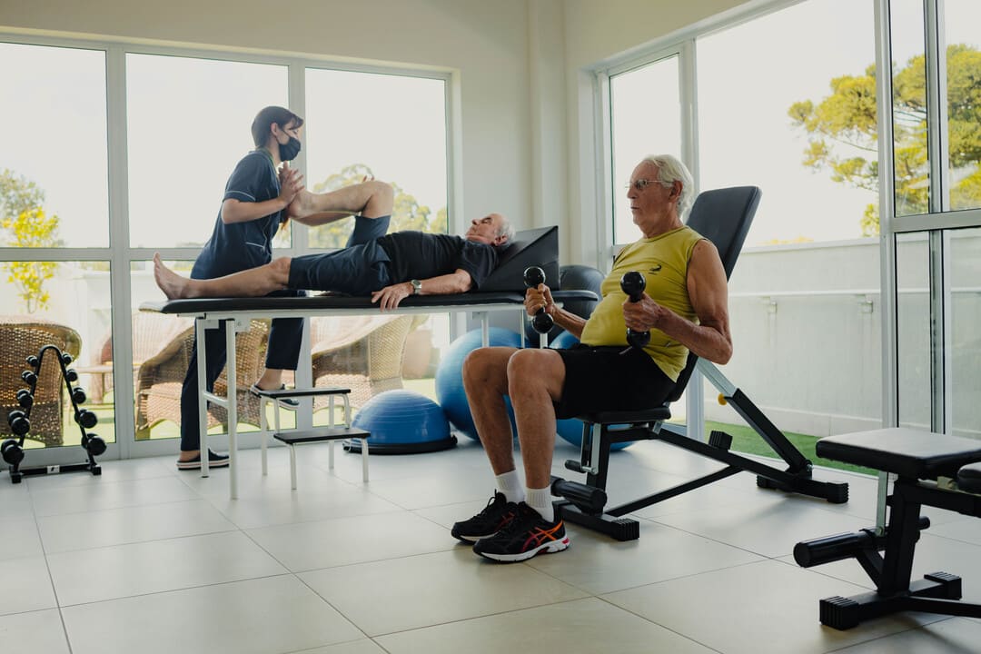 Idosos realizando fisioterapia e exercícios em uma unidade de transição da Versania, acompanhados por profissional da saúde.