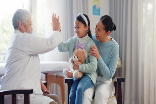 Profissional de saúde interage de forma lúdica com uma criança em unidade de transição pediátrica, ao lado de um familiar.